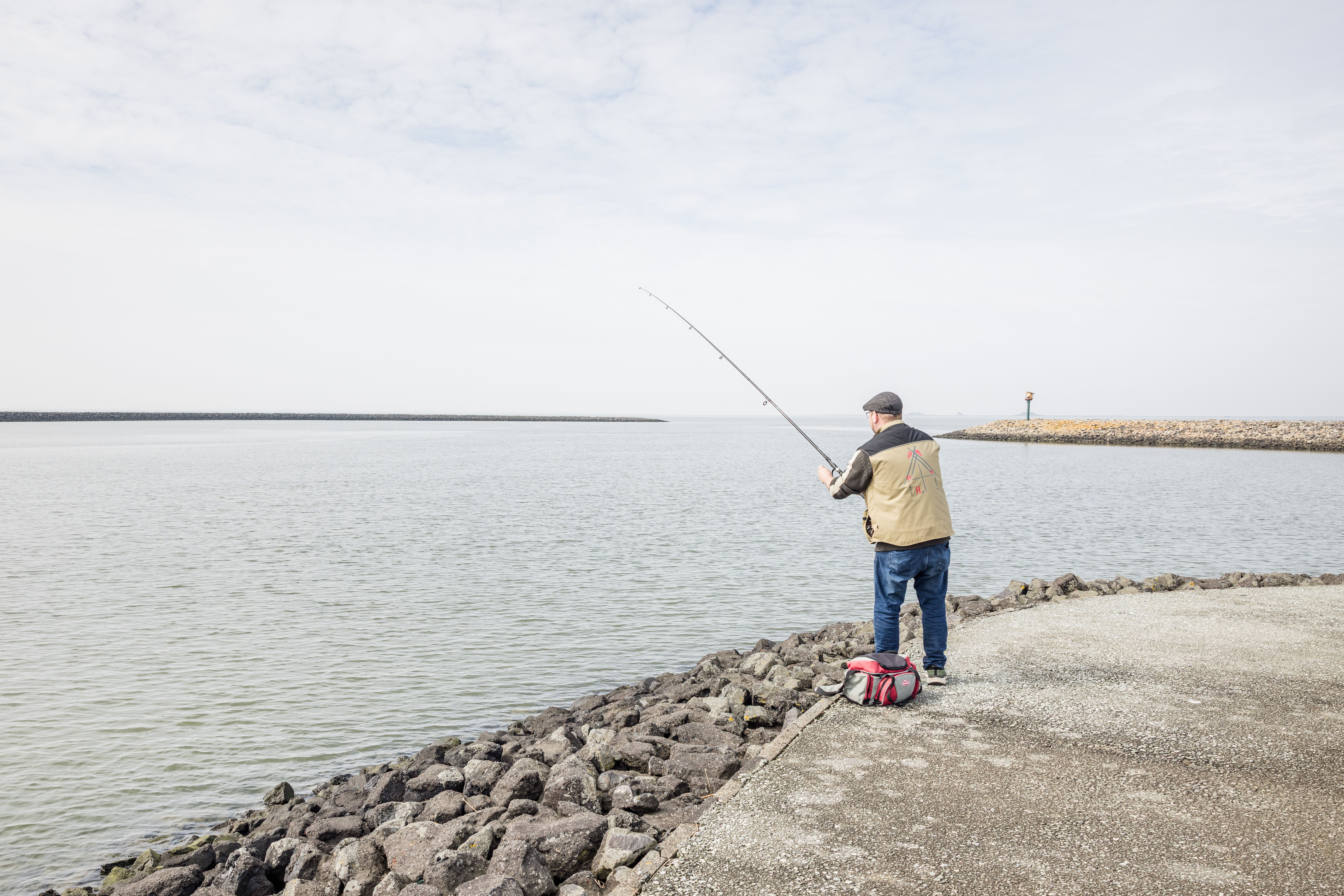 Ein Mann steht am Ufer der Nordsee und angelt. 