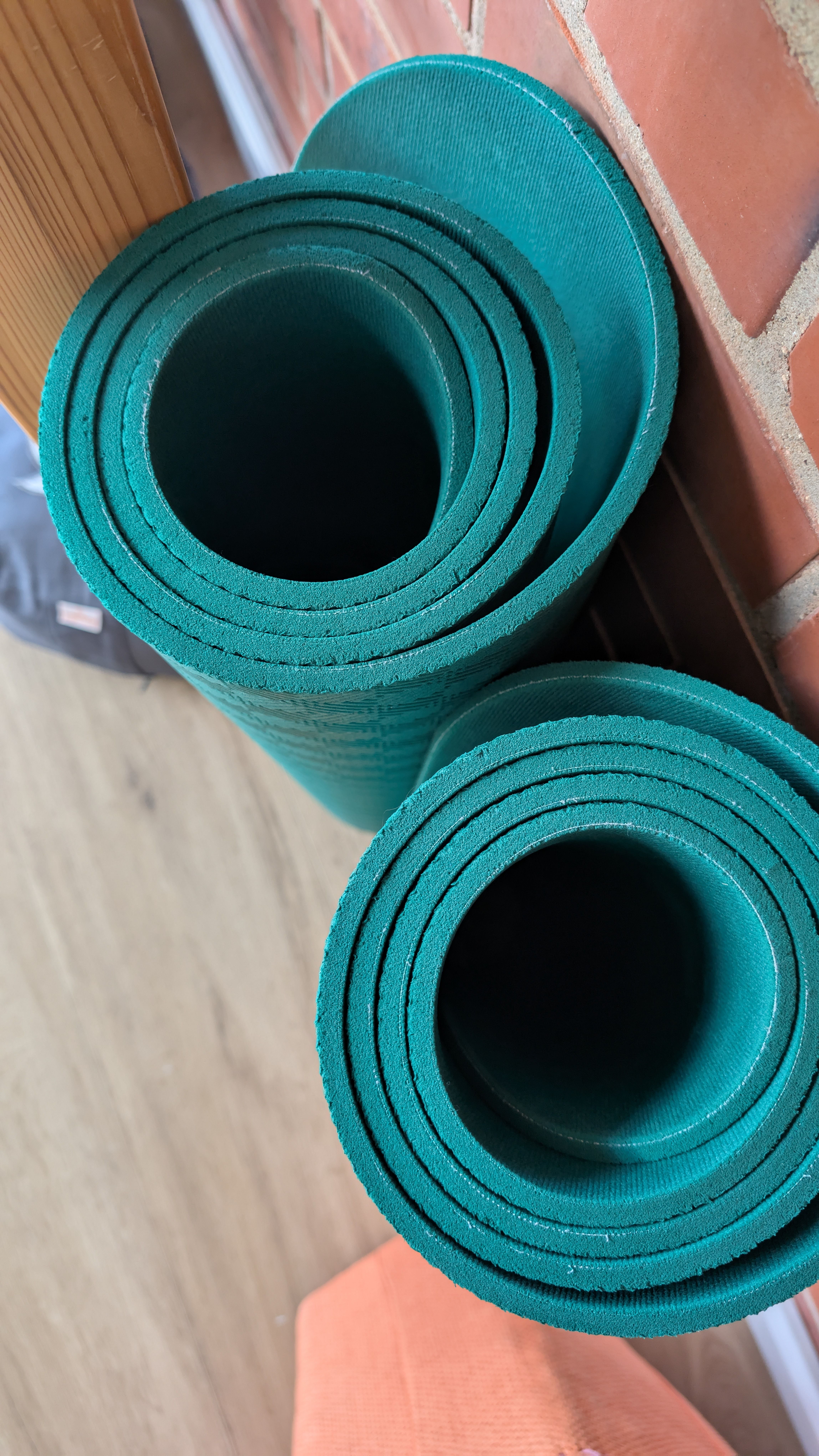 Blick von oben auf zwei türkise Yogamatten vor einer Backsteinwand. 