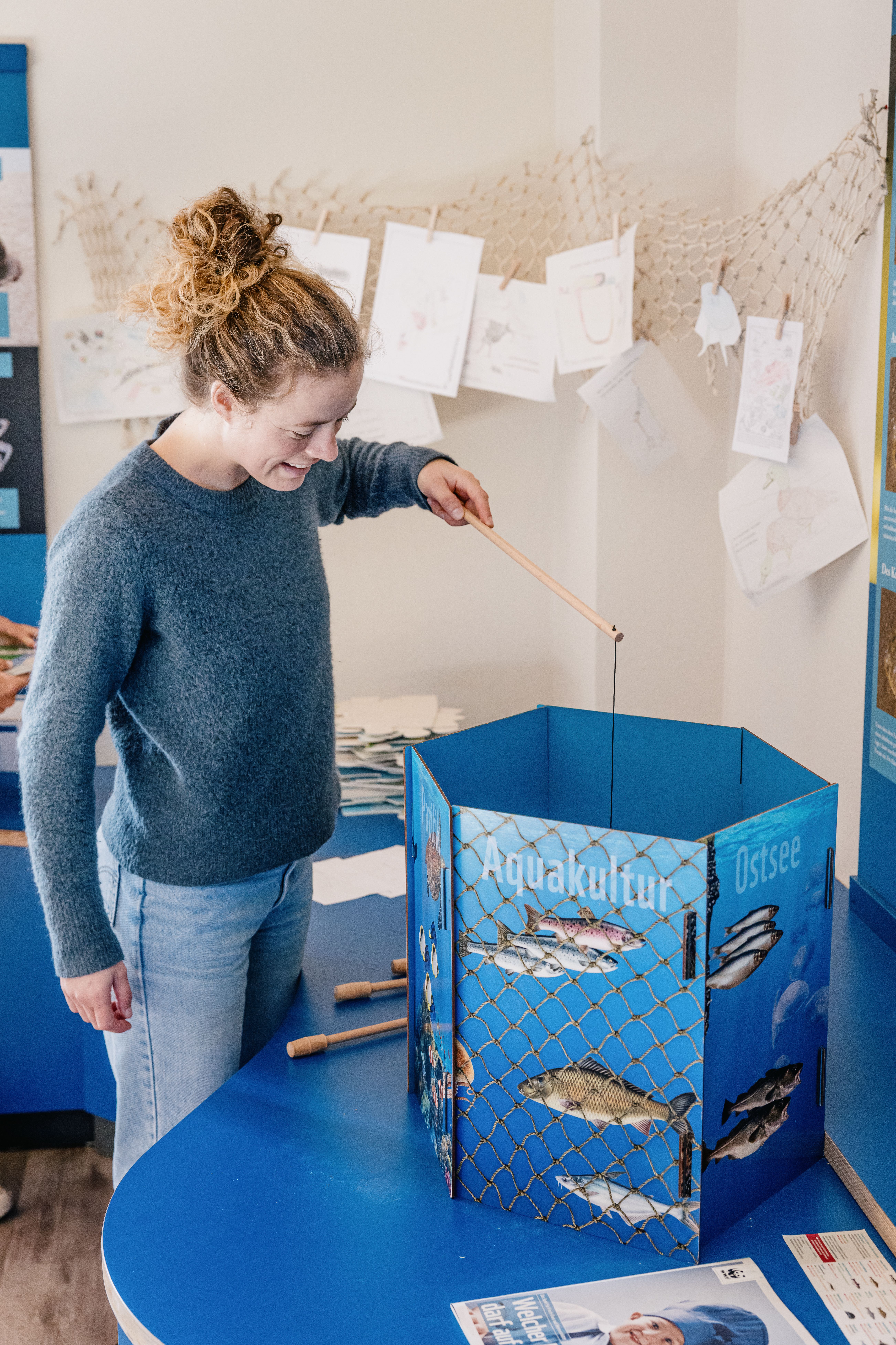Eine Frau im blauen Pullover und Jeans angelt spielerisch Objekte in der Ausstellung des Nationalpark Hauses Nordstrand. 