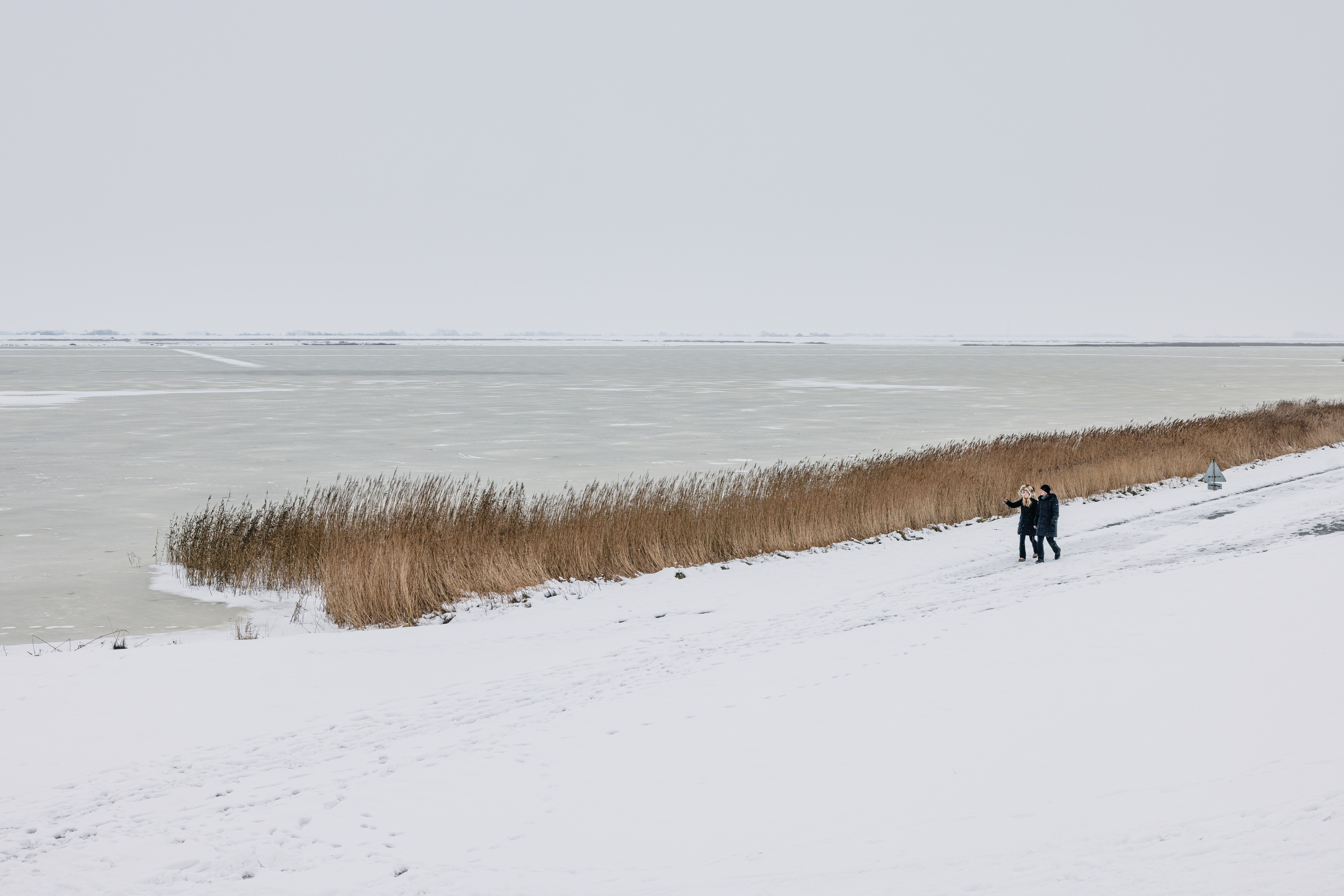 Ein Paar spaziert bei Schnee am Deich. 