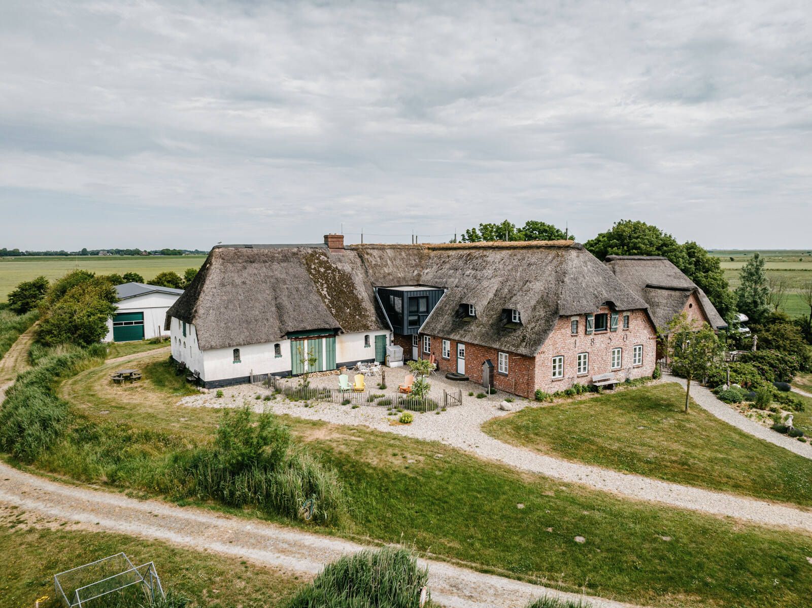 Blick aus der Vogelperspektive auf ein großes, reetgedecktes Haus. Verlinkung auf Unterseite "Übernachten auf Nordstrand".