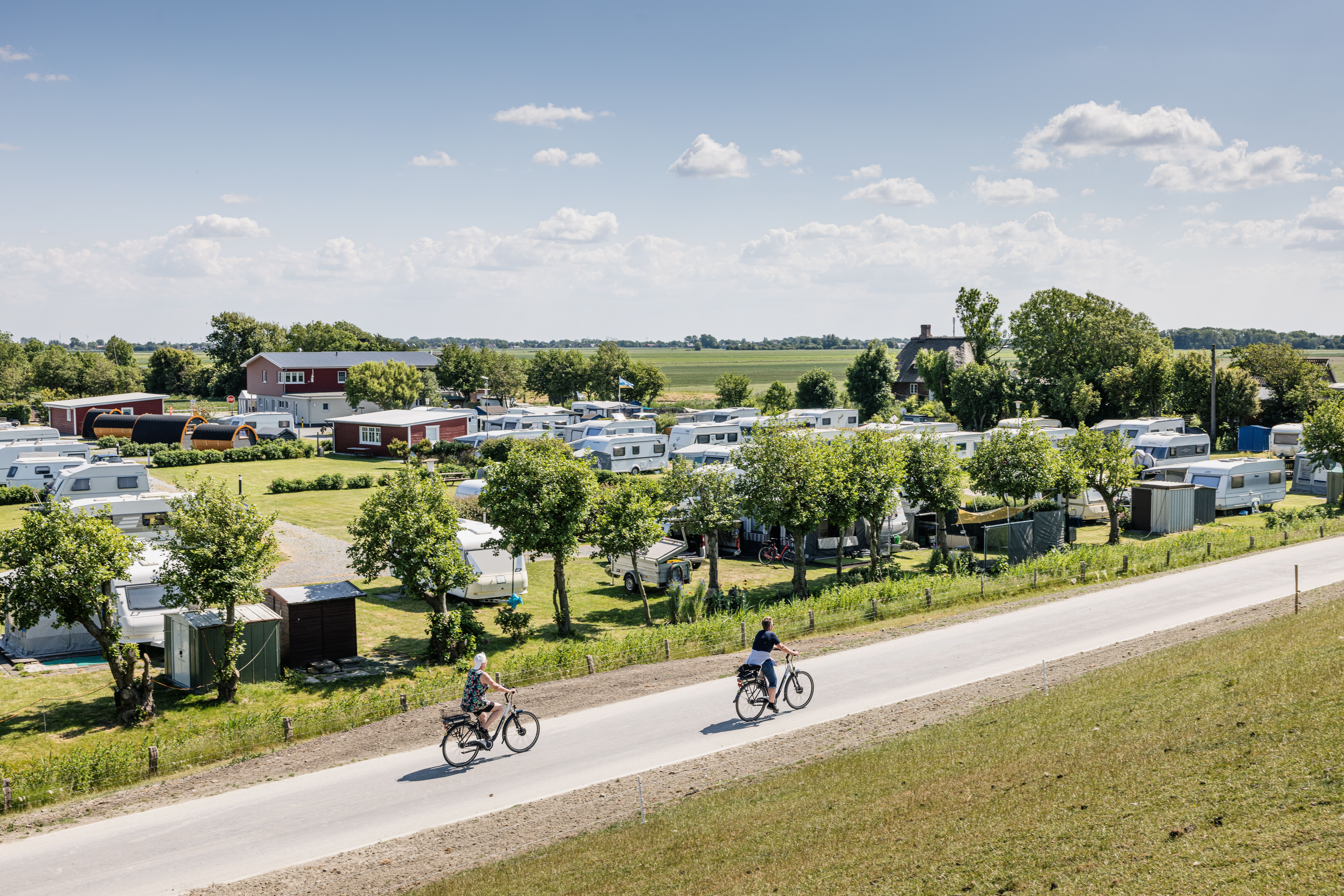 Zwei Radfahrer fahren auf einem Weg entlang eines Campingplatzes bei Sonnenschein.
