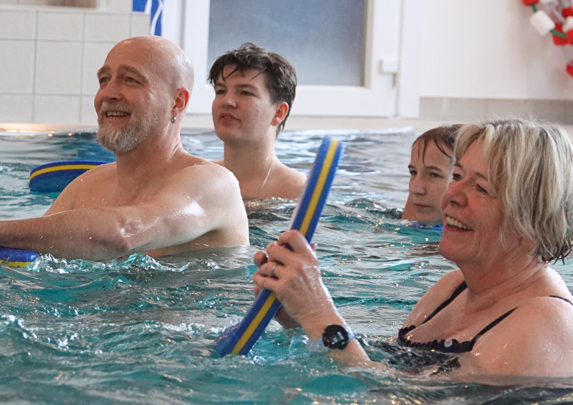 Personen stehen bei Aquafitness im Wasser und machen Übungen mit einem Schwimmbrett. 
