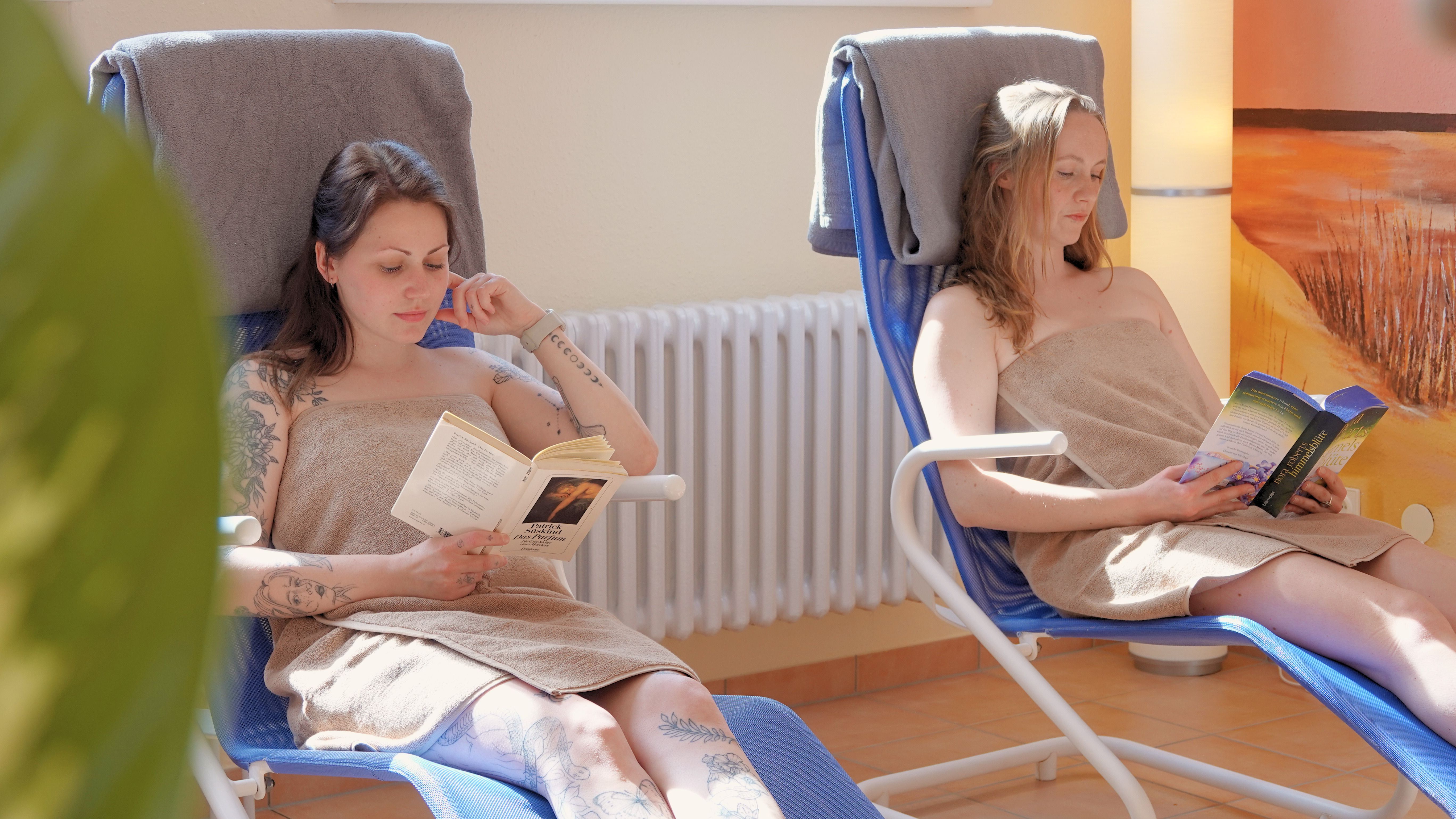 Zwei Frauen sitzen auf einer blauen Liege und lesen. 