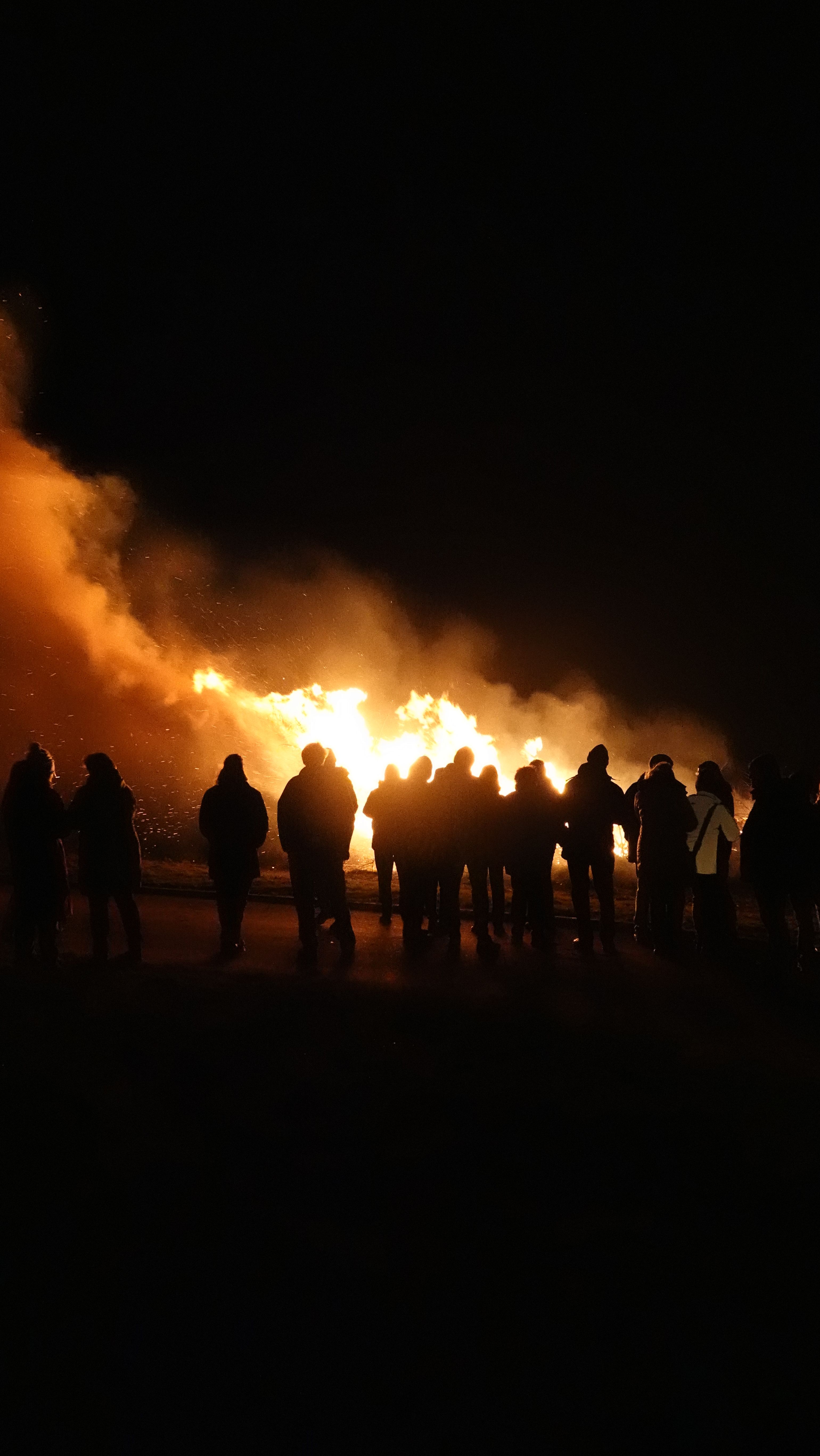 Menschen stehen vor einem großen Lagerfeuer. 