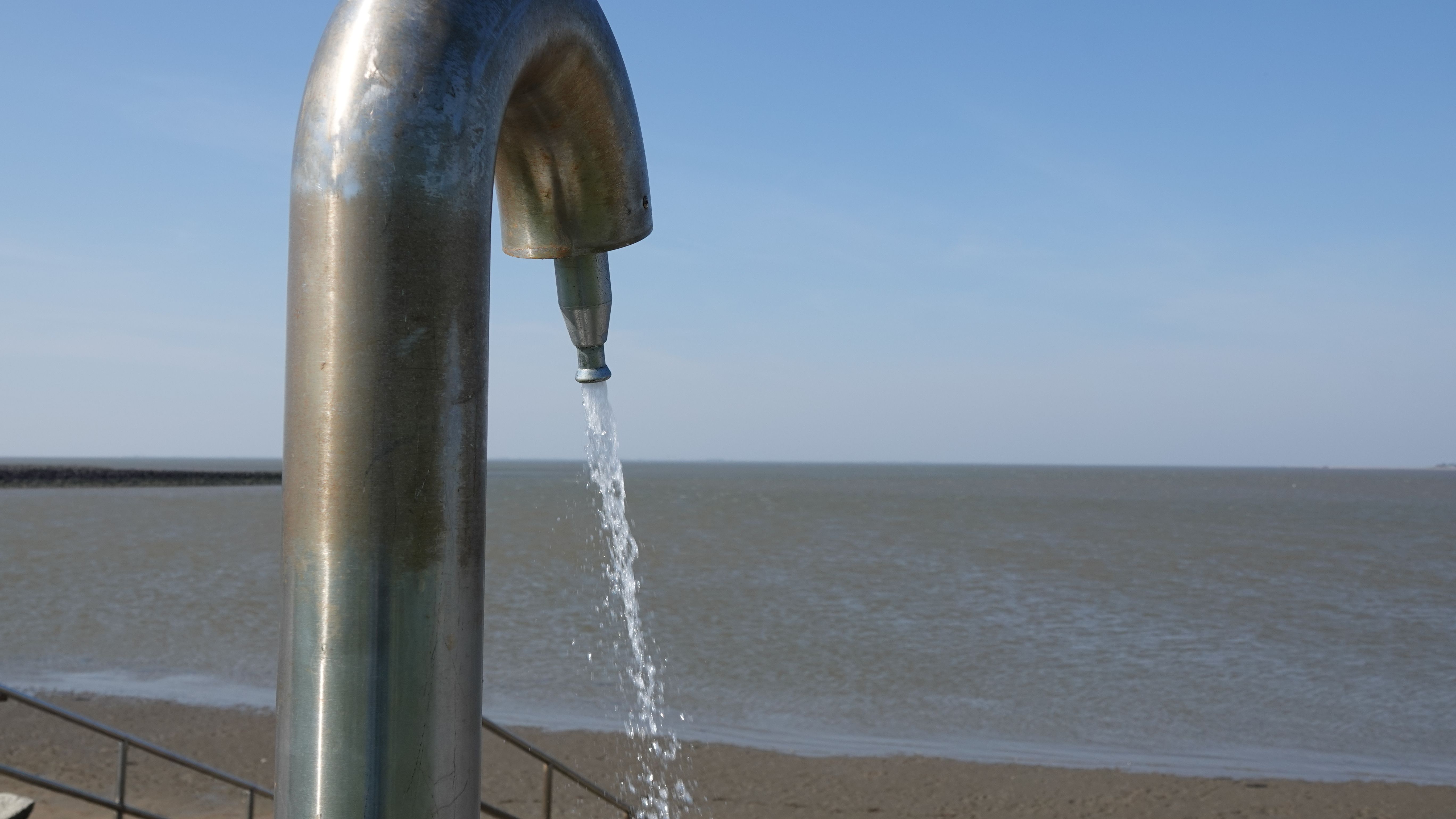 Aus einer Außendusche am Meer fließt Wasser. 