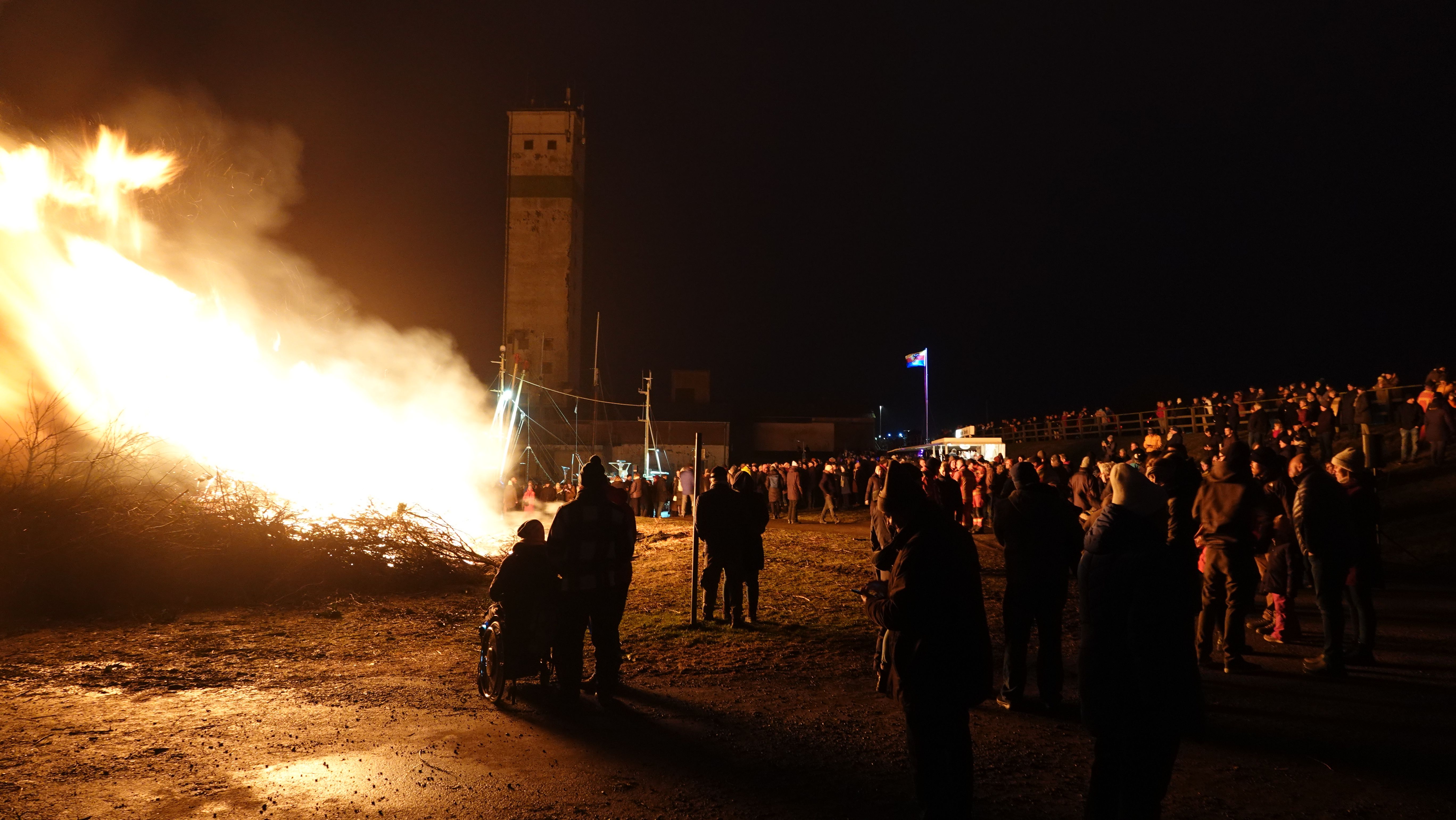 Menschen stehen um das Biikefeuer am Süderhafen auf Nordstrand