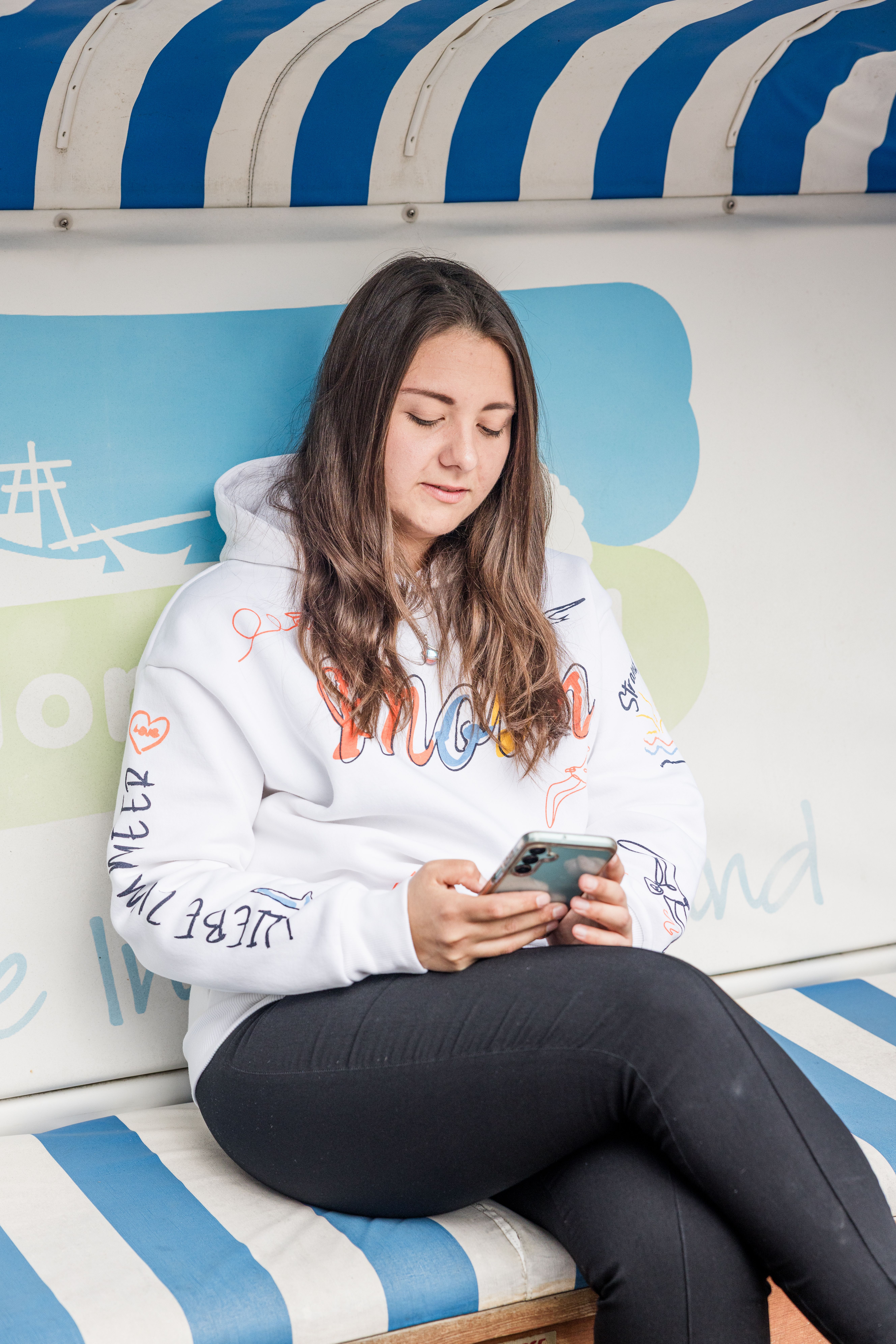 Eine Dame sitzt in einem Strandkorb und hält ein Handy in der Hand.