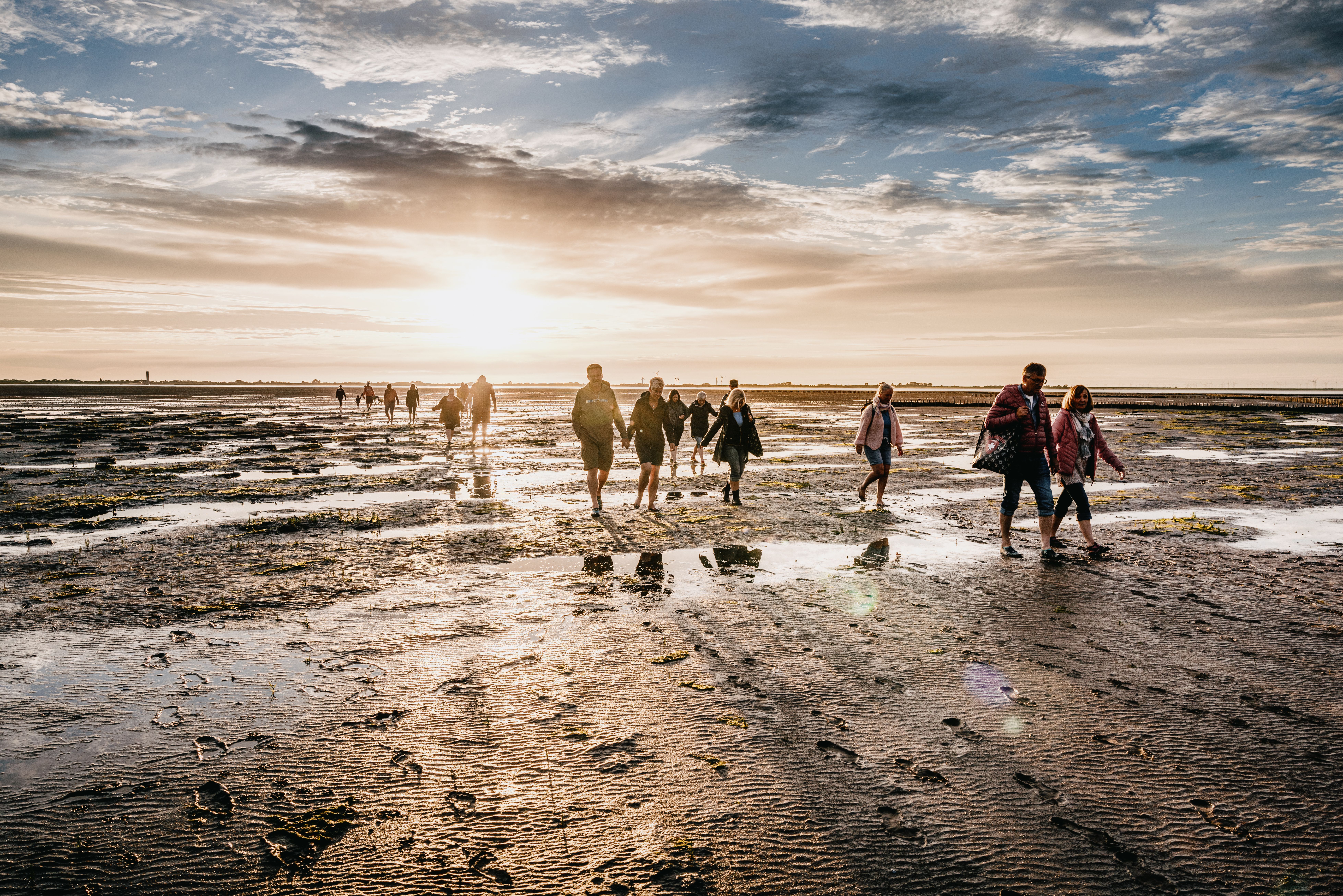 Eine Gruppe läuft bei Sonnenuntergang durchs Watt.