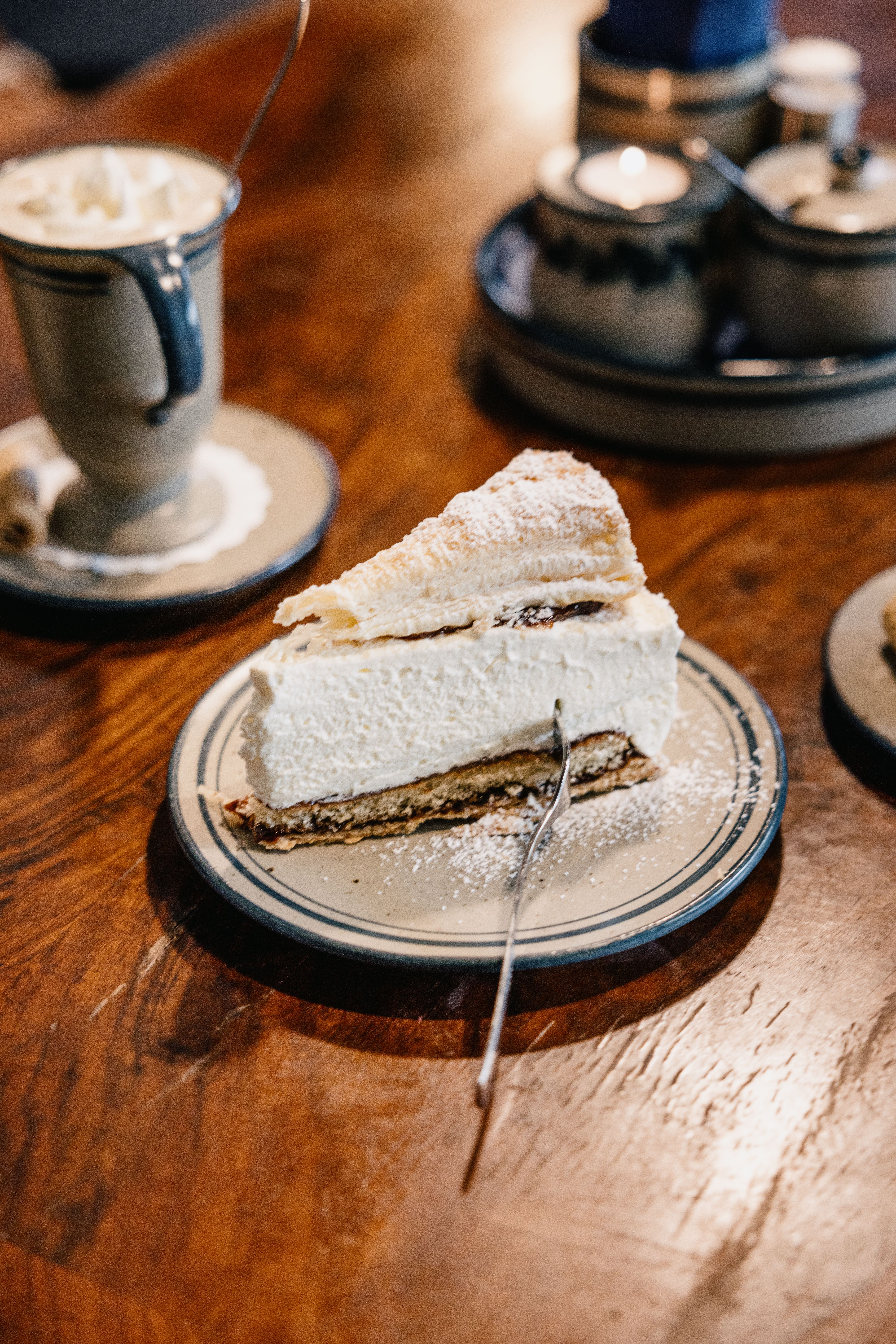 Ein Stück Friesentorte mit Gabel in der Torte liegt auf einem Teller, daneben eine Tasse Pharisäer. 