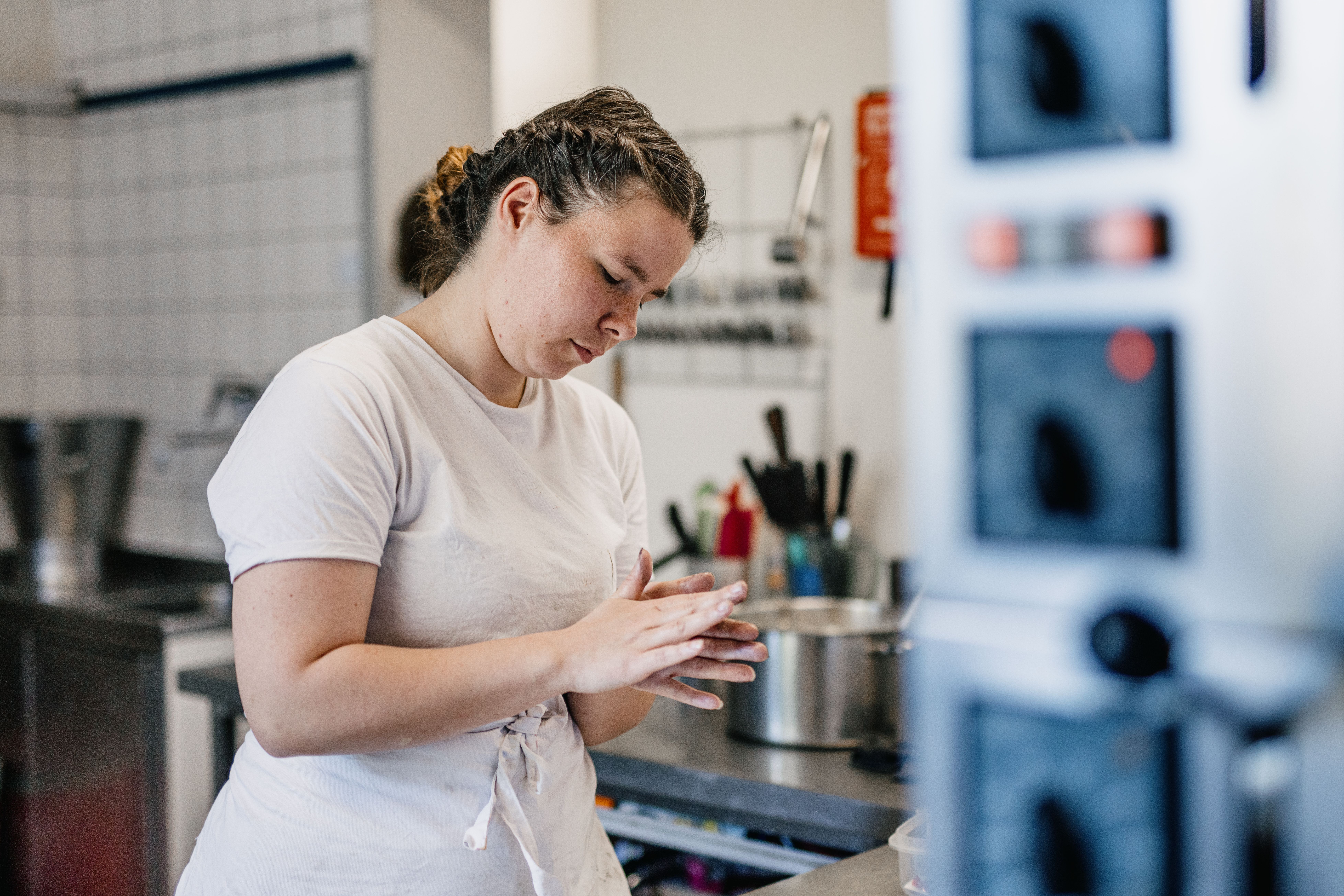 Eine junge Frau steht in einer Gastro-Küche und formt etwas in ihren Händen. 