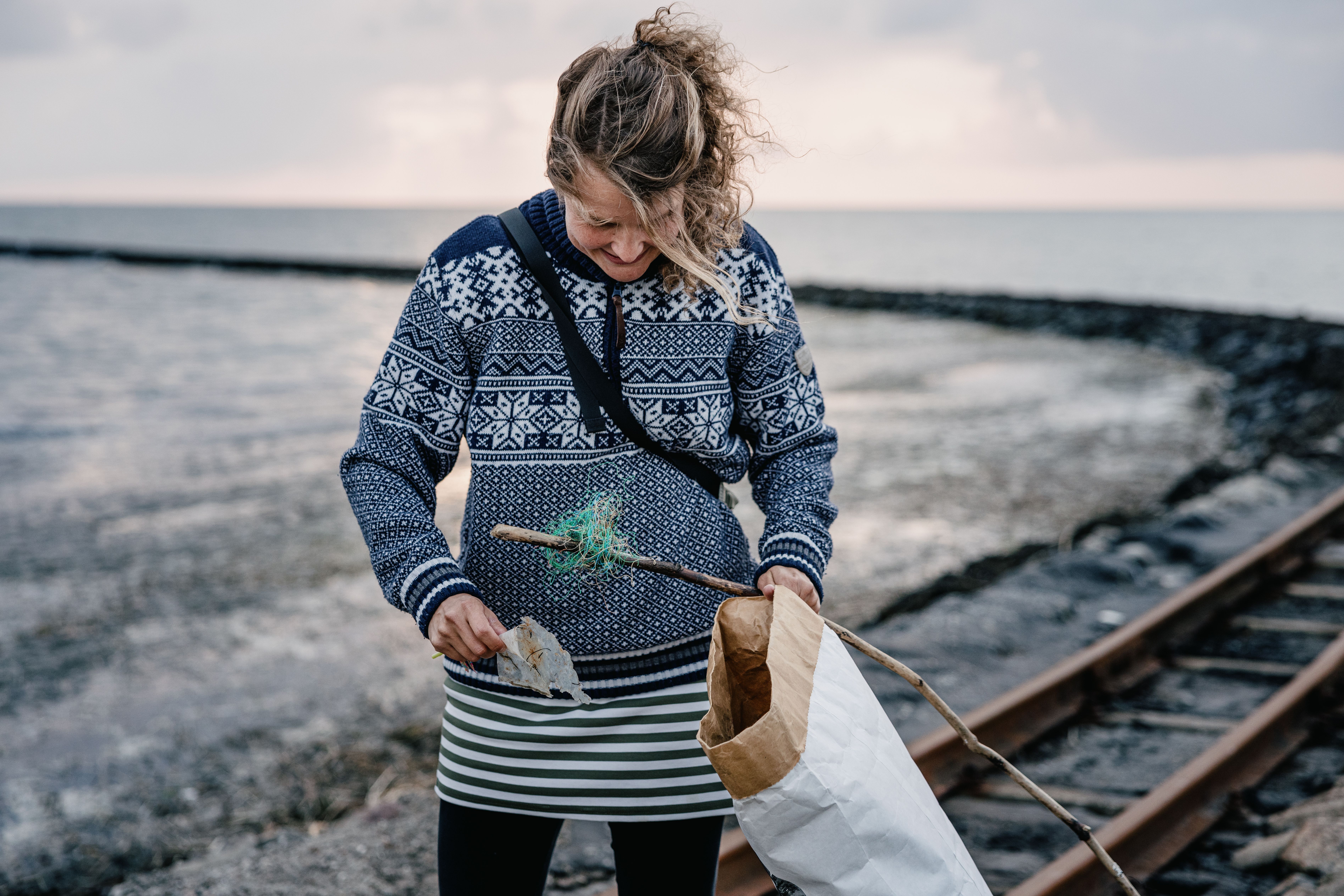 Eine Frau sammelt an der Nordsee herumliegenden Müll.