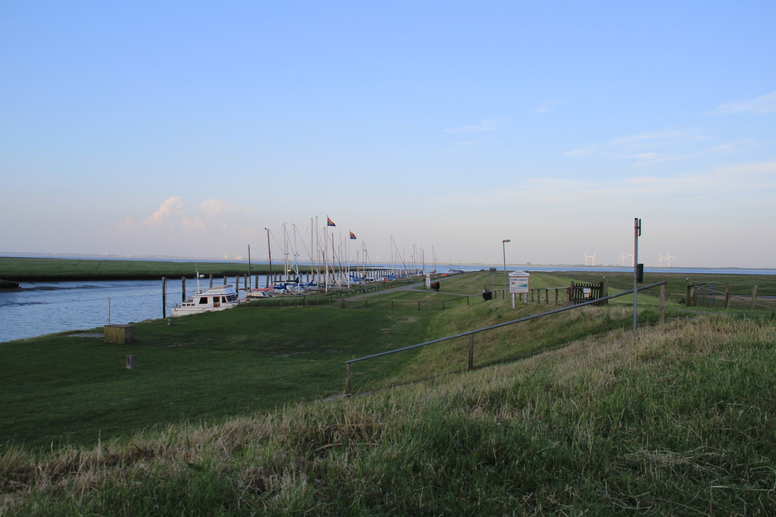 Blick vom Deich auf Nordstrand, im Hintergrund liegen einige Schiffe in einem kleinen Hafen