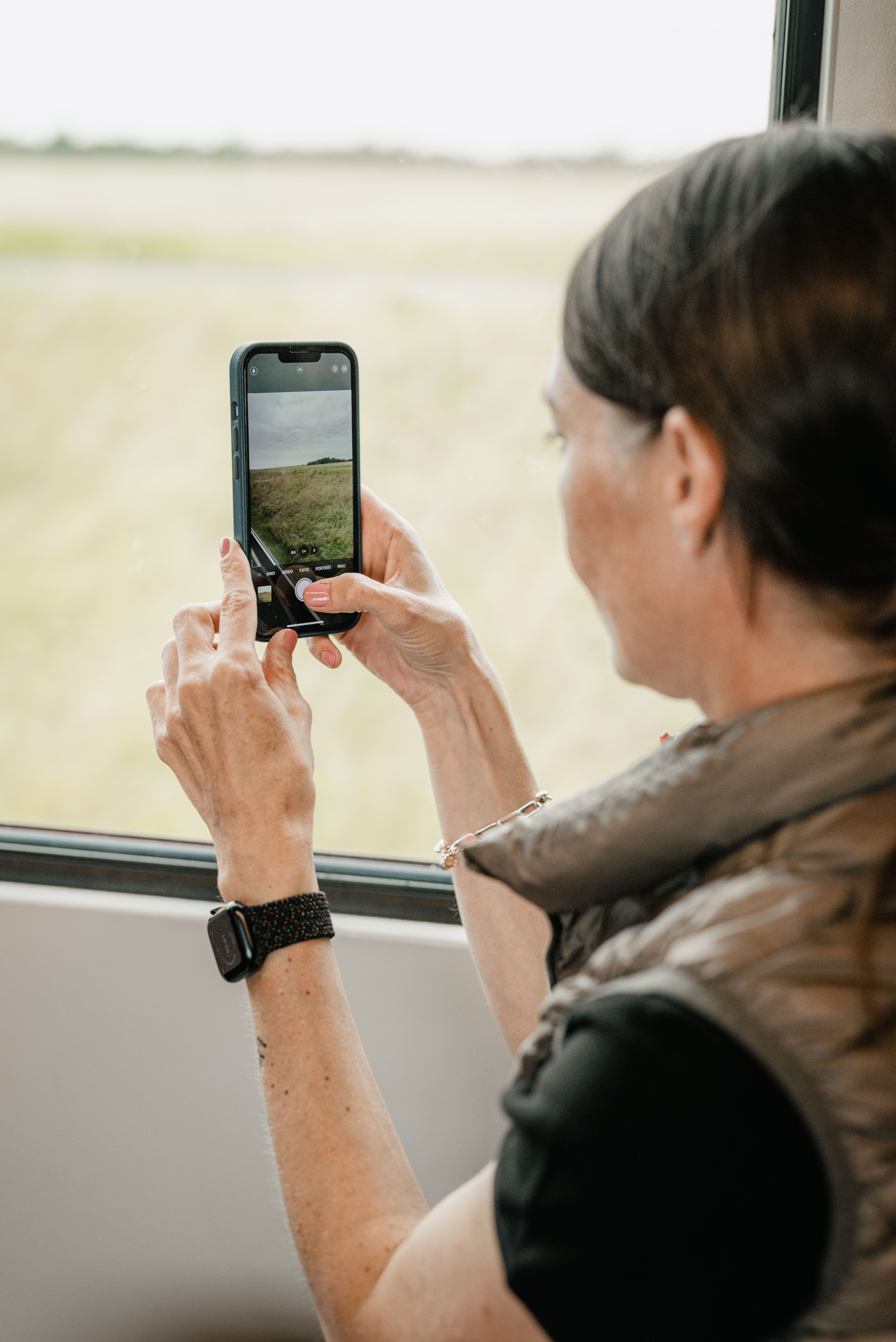 Eine Dame sitzt drinnen und macht mit ihrem Smartphone ein Bild von der Landschaft draußen.