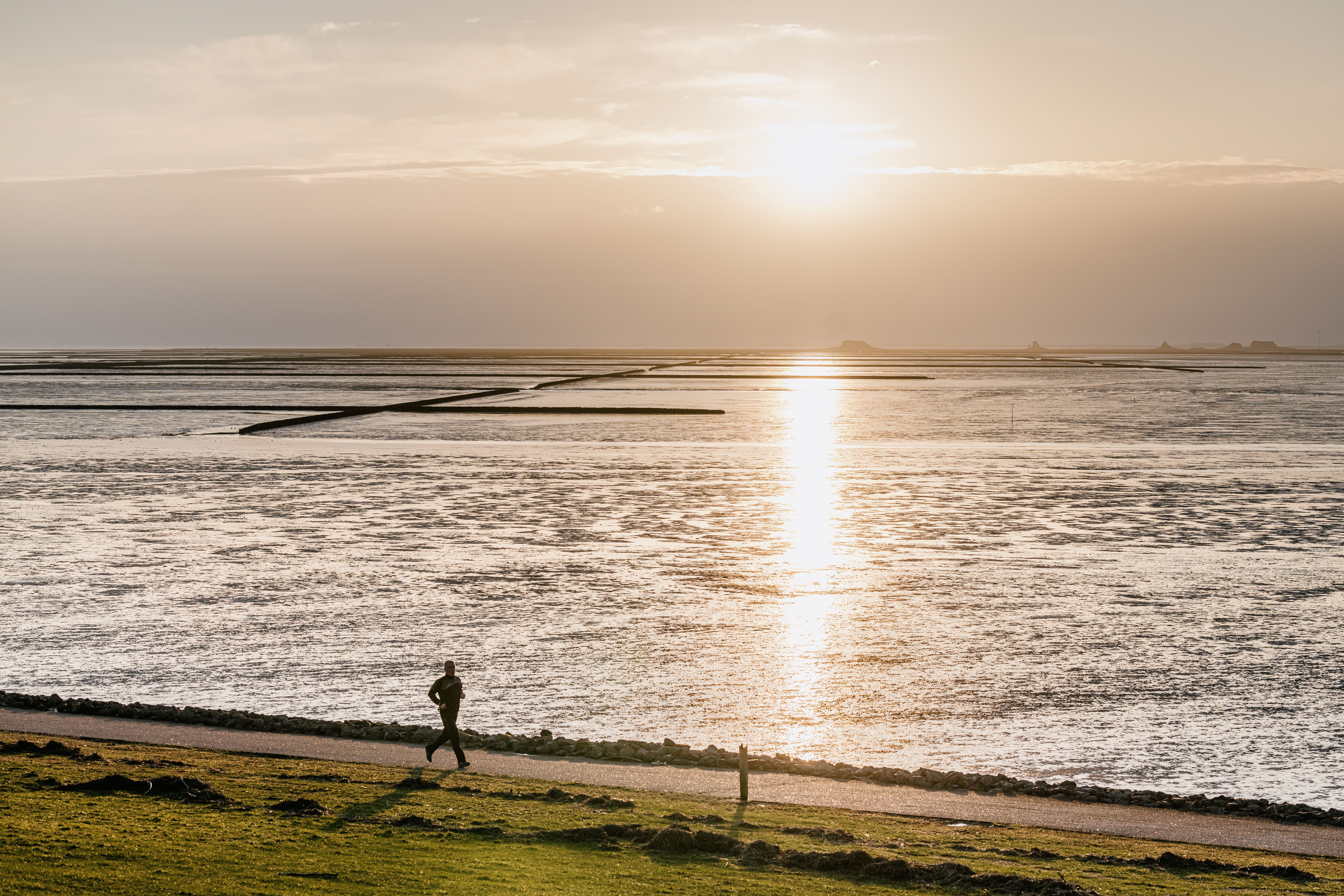 Eine joggende Person vor dem Wattenmeer im Sonnenuntergang