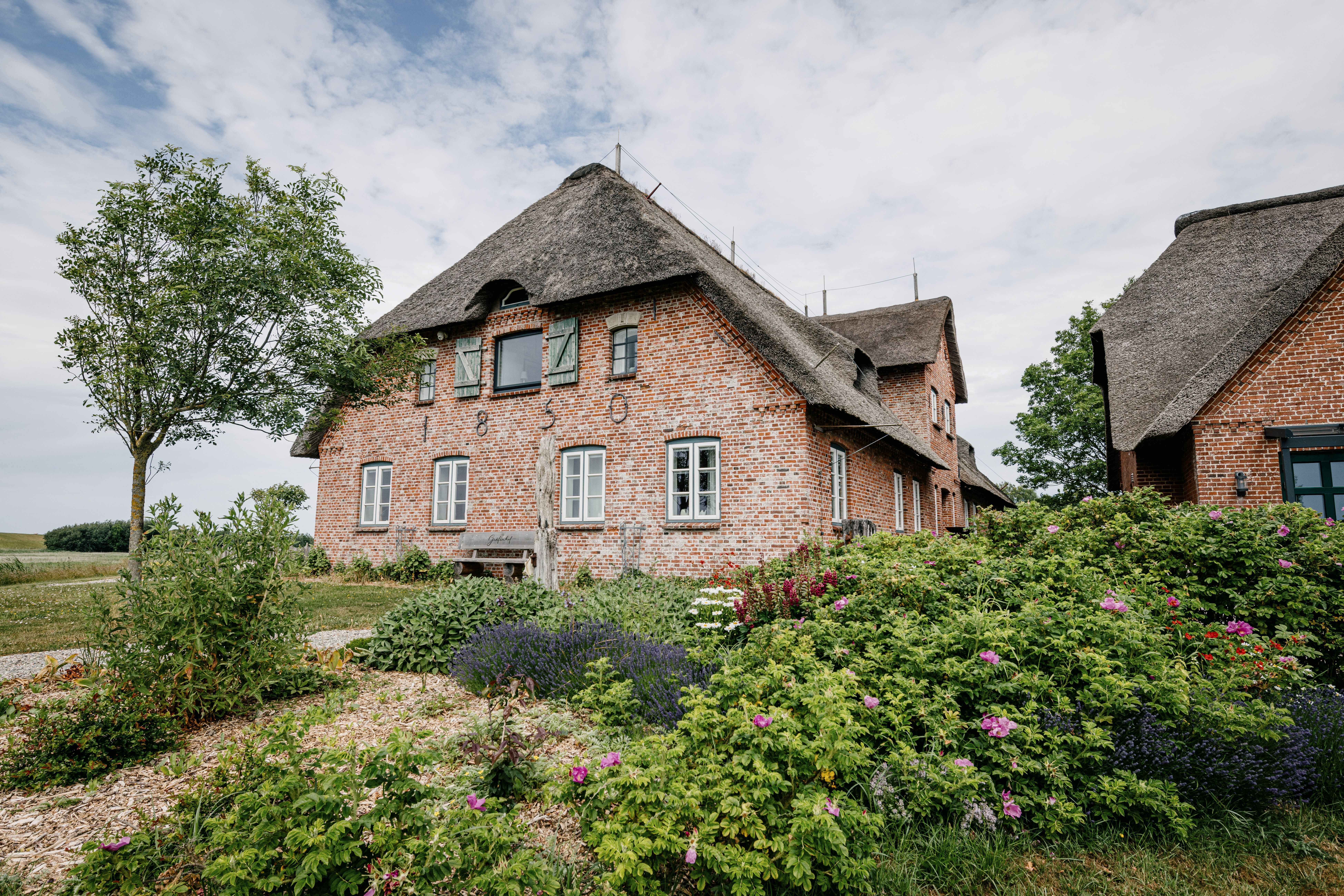 Ein reedgedecktes Haus mit Backsteinen im Grünen. Verlinkung auf Unterseite "Ferienwohnung"