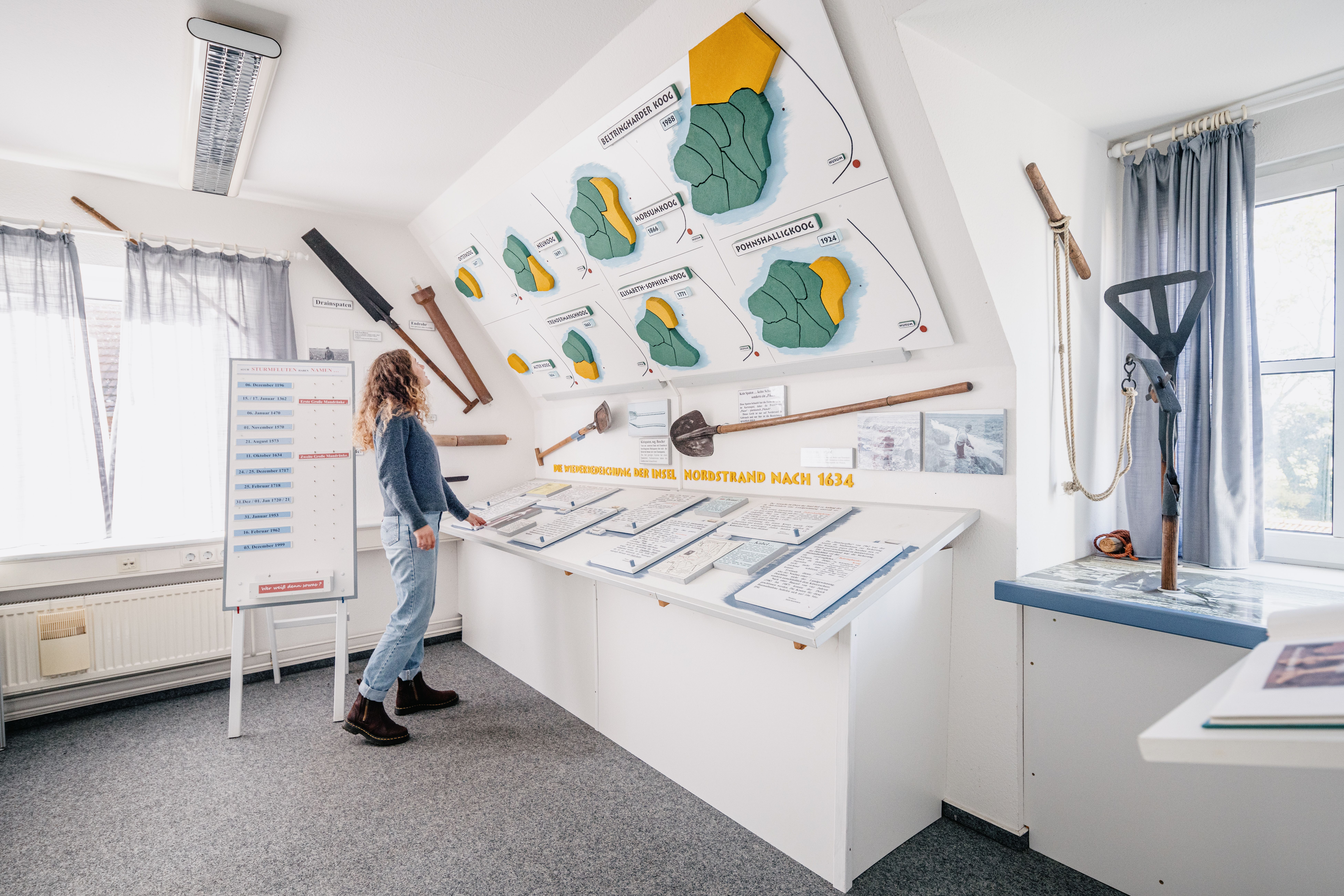 Eine Frau schaut sich Informationstafeln über die Entstehung Nordstrands an einer Wand an. 