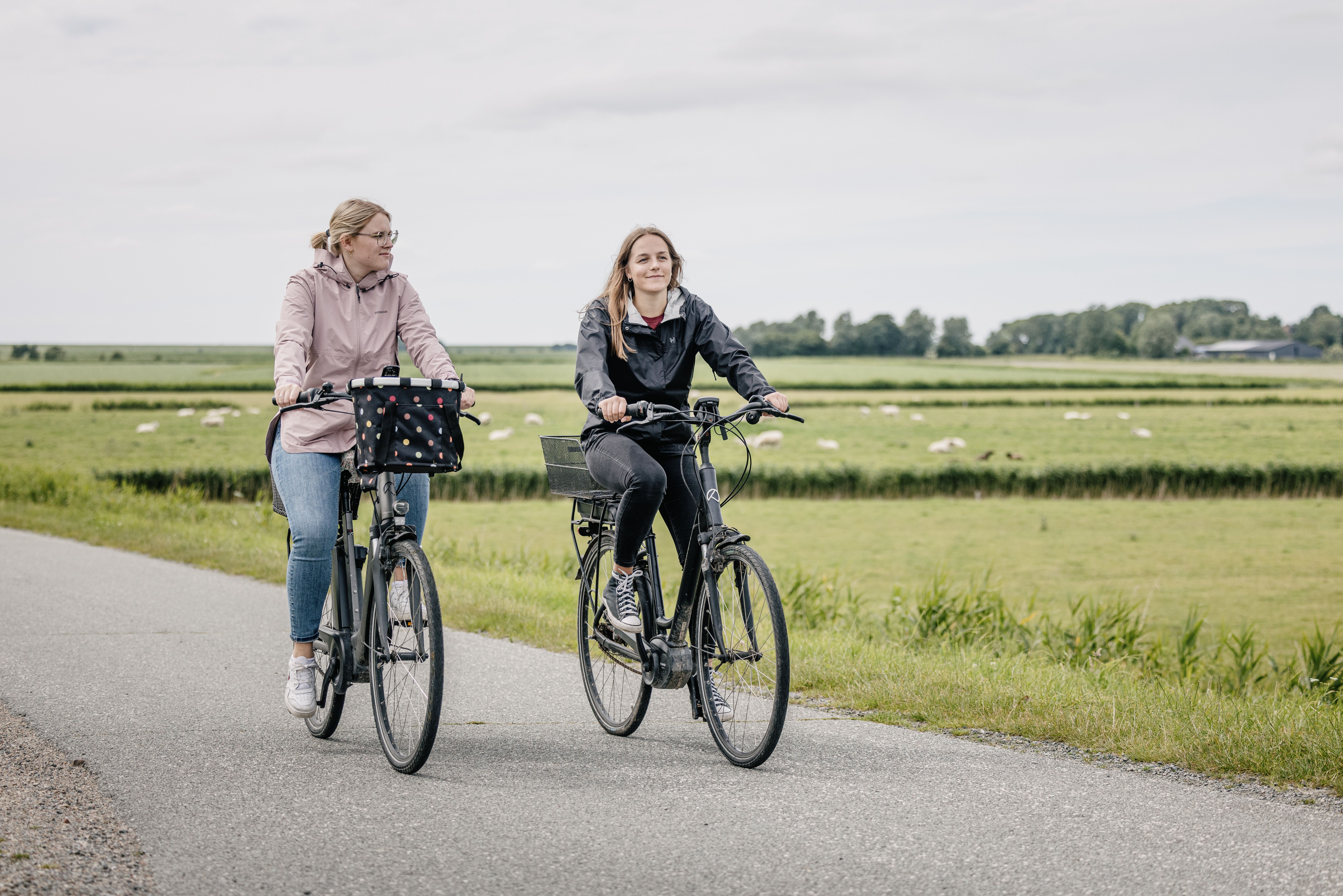Zwei junge Frauen mit dem Fahrrad an Wiesen vorbei. 