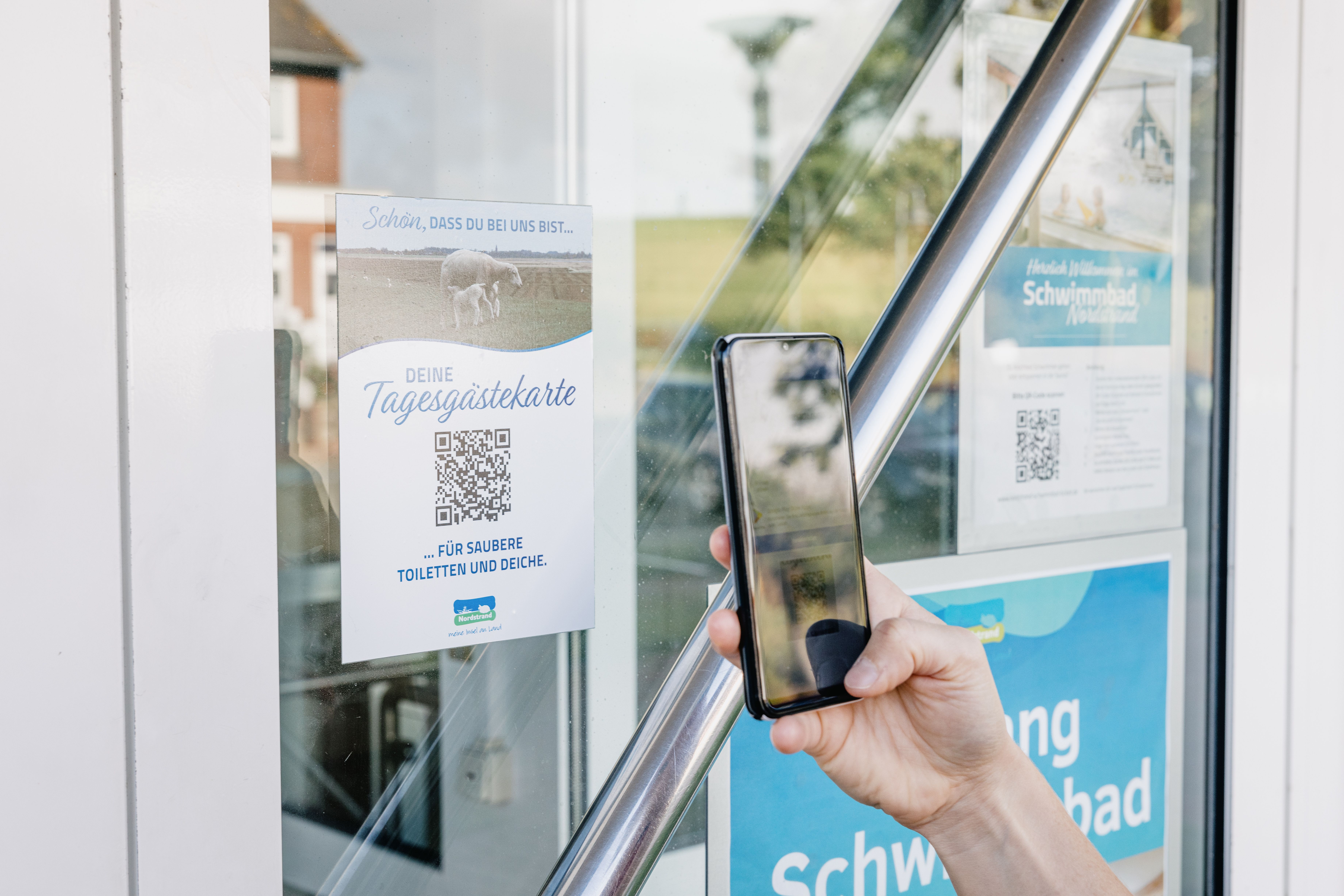 Eine Hand hält ein Handy und scannt QR COde für die Tagesgästekarte auf Nordstrand. 